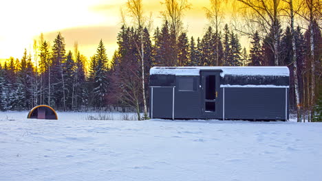 still shot of a cabin and barrel sauna covered in snow with dramatic sky