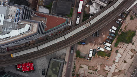 Aerial-birds-eye-overhead-top-down-ascending-view-of-turning-double-track-railway-line-leading-elevated-through-urban-neighbourhood.-Two-train-passing-each-other.-London,-UK