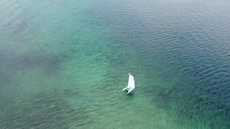 A-aerial-view-of-a-small-sailboat-in-the-blue-of-the-Caribbean-waters-on-a-sunny-day