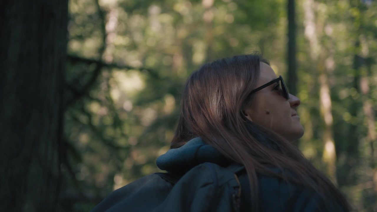 Il sole splende su una giovane escursionista con uno zaino che cammina nel bosco.