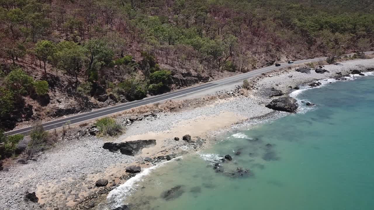 antena de drones siguiendo autos y panorámica hacia arriba para revelar agua tropical azul