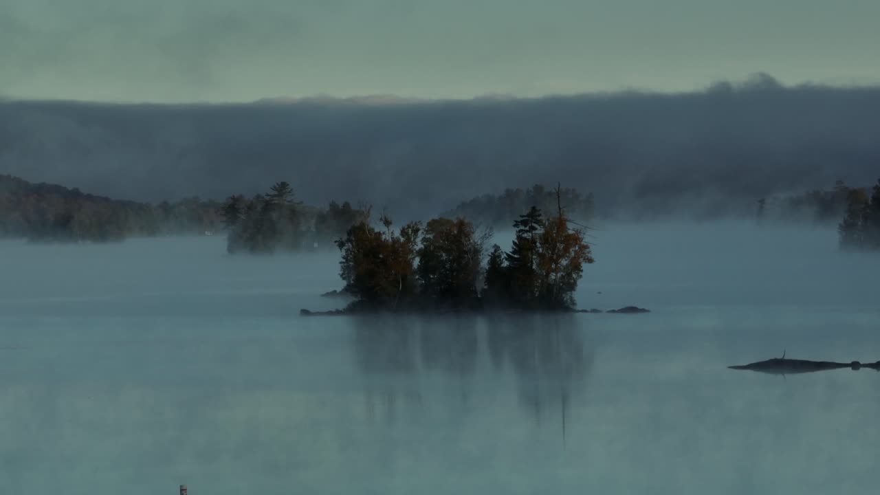 Spectacular aerial dawn fog surrounds lake island Slow-Motion Aerial