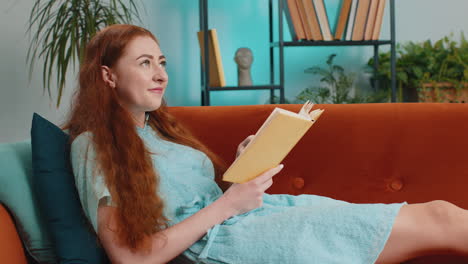 young woman relaxing interesting book turning pages smiling enjoying literature taking rest on sofa