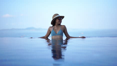 Mujer-Hermosa-Y-Elegante-Con-Traje-De-Baño-De-Moda-Sentada-En-Una-Piscina-Infinita,-Fondo-Borroso,-Luz-Suave