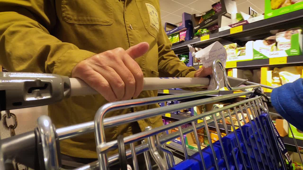 A man briskly pushing a shopping cart in a hurry, tapping his thumb. Close up.