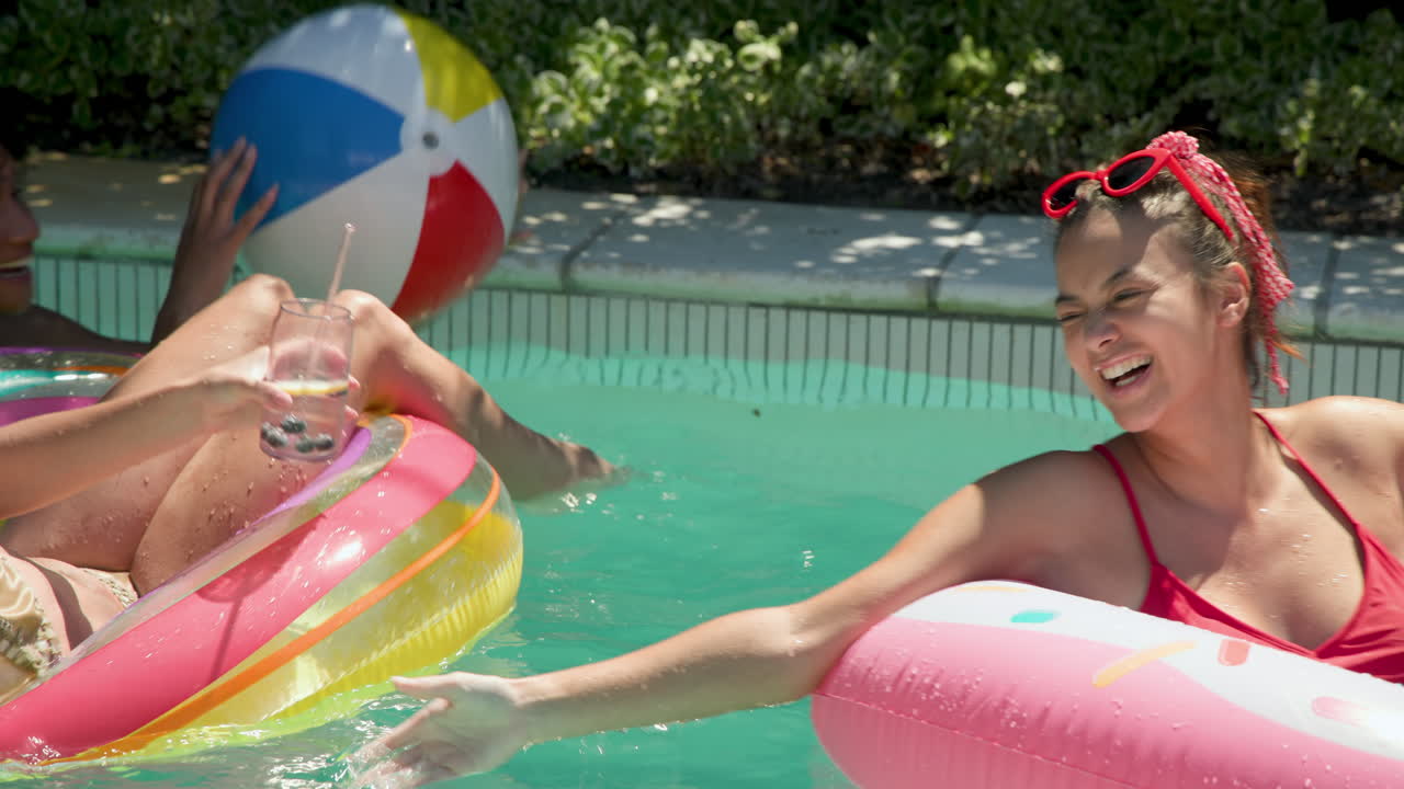 Diverse female friends enjoying sunny day by pool, laughing and splashing water playfully