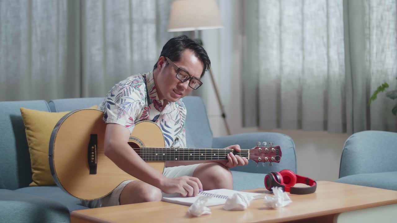 기타를 은 종이를 가지고 있는 아시아인 작곡가가 집에서 음악을 작곡하는 동안 두통을 고 버립니다.