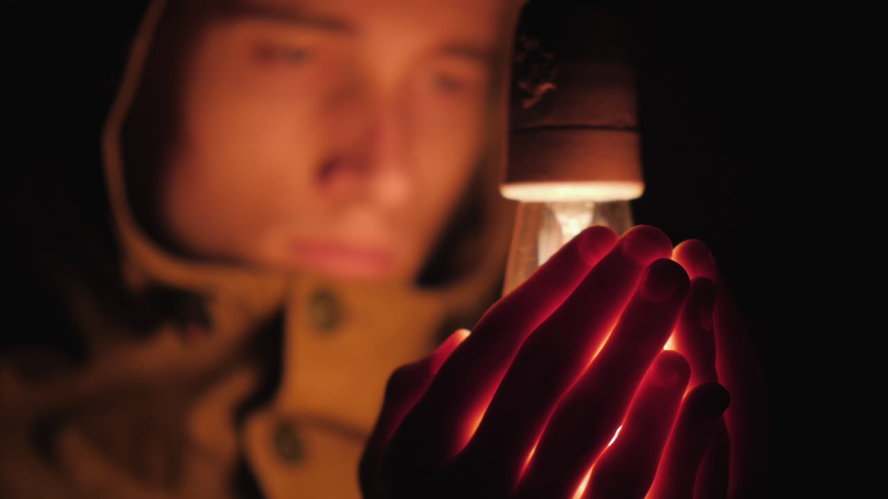 hombre triste calienta sus manos cerca de una bombilla en la oscuridad