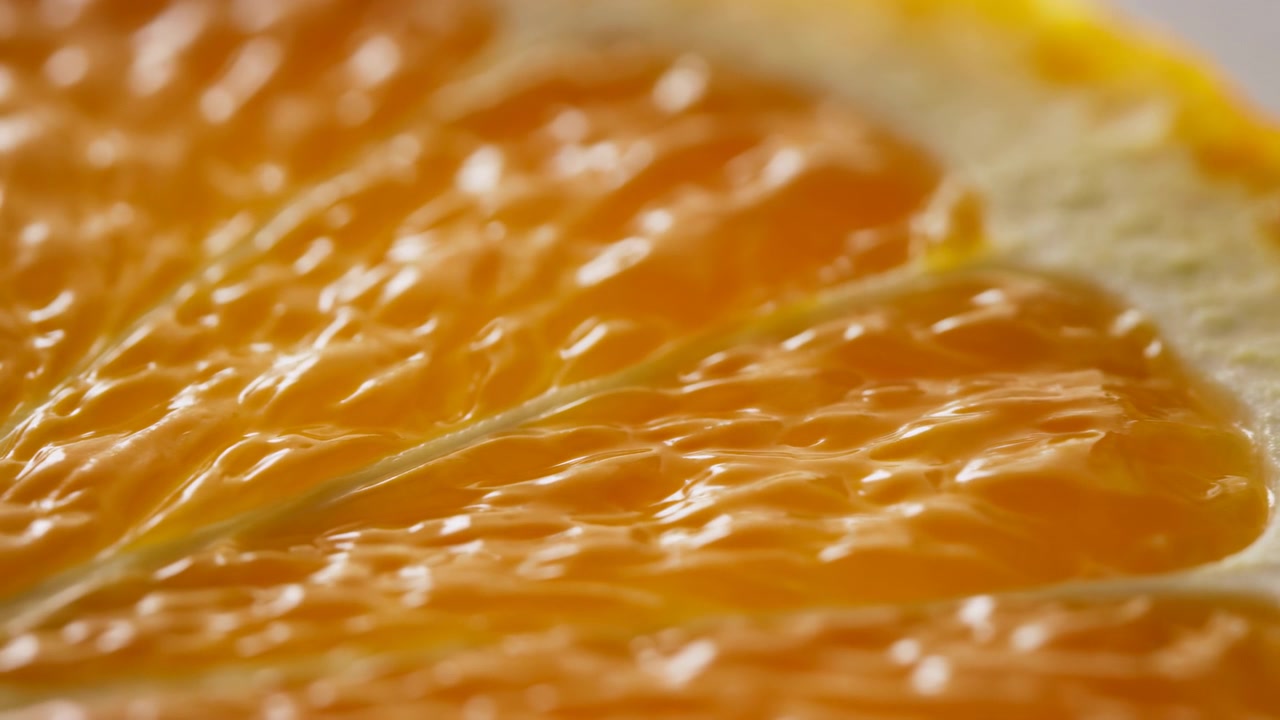 Primo piano di uno spicchio d'arancia che luccica di succo, texture della polpa altamente dettagliata, bordo della buccia luminoso, luce soffusa da studio