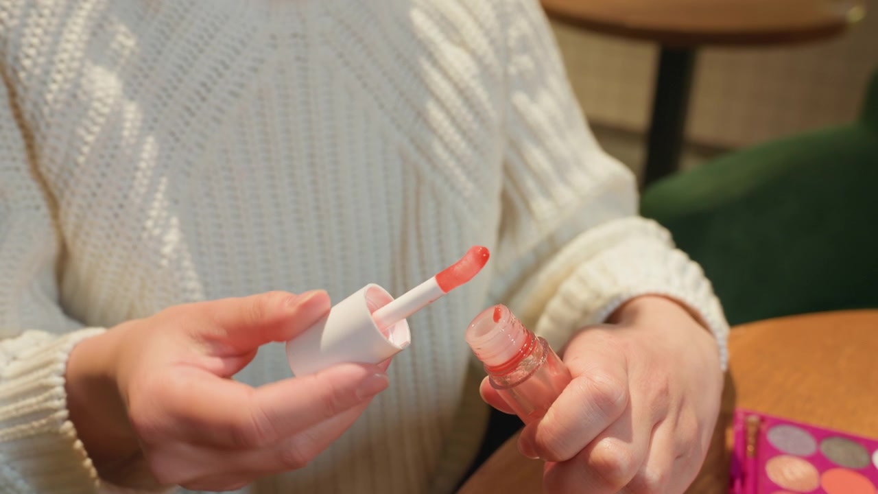 Primo piano di mani femminili che aprono una boccetta di lucidalabbra