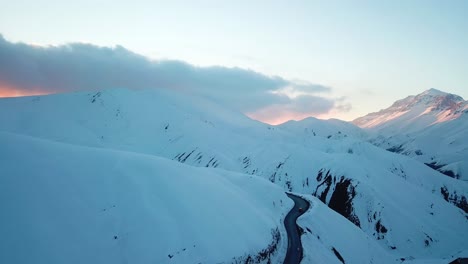 Hermosa-Puesta-De-Sol-Sobre-Una-Alta-Montaña-Cubierta-De-Nieve-En-La-Cordillera-De-Alborz,-Clima-Del-Cáucaso-En-La-Temporada-De-Invierno,-Paisaje-Escénico-De-Naturaleza-Salvaje,-Nevadas-épicas-Naturales,-Asfalto,-Carretera-Sinuosa,-Conducción-De-Vehículos