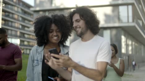 cheerful friends looking at smartphone during stroll.