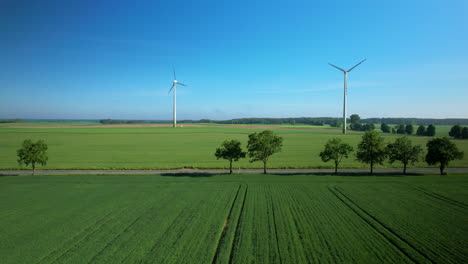 push in aerial view sustainable wind turbines spinning on sunny lush rural agricultural farmland