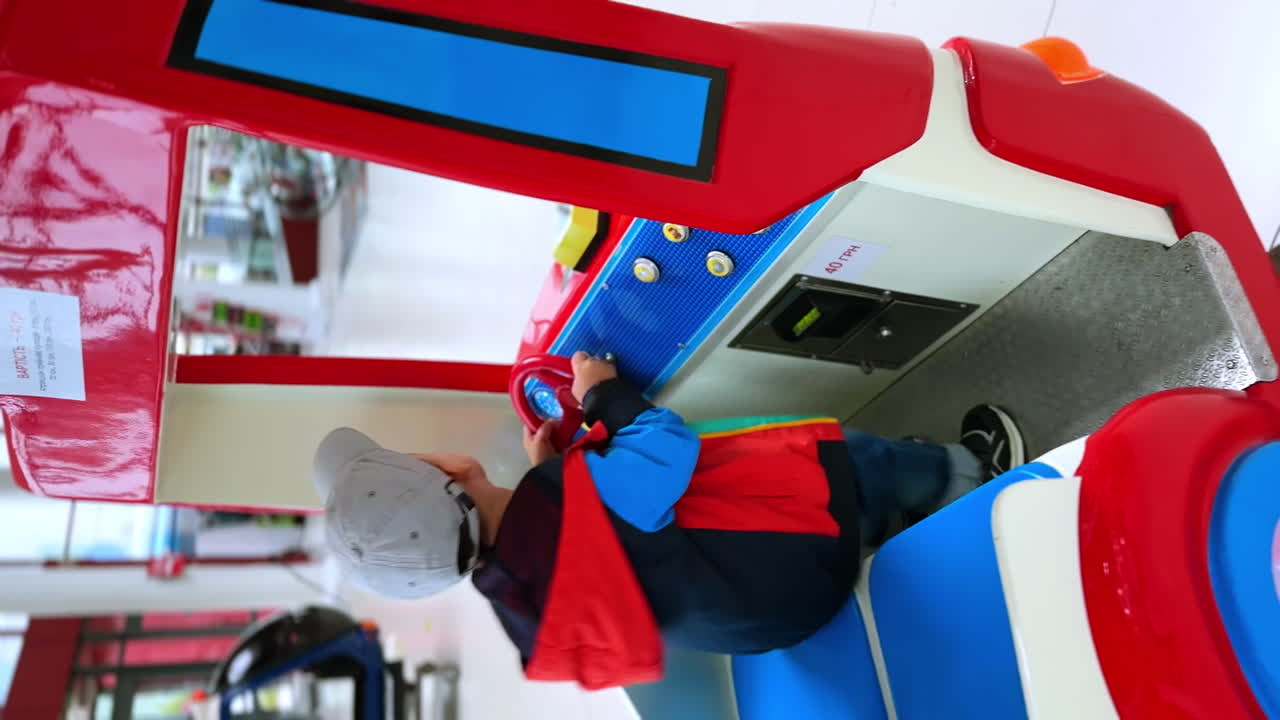 Excited little toddler boy jumping inside the toy machine. Kid turns the wheel and looks around actively. Vertical view.