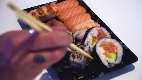 defocused hand picks sushi roll from assorted platter with chopsticks