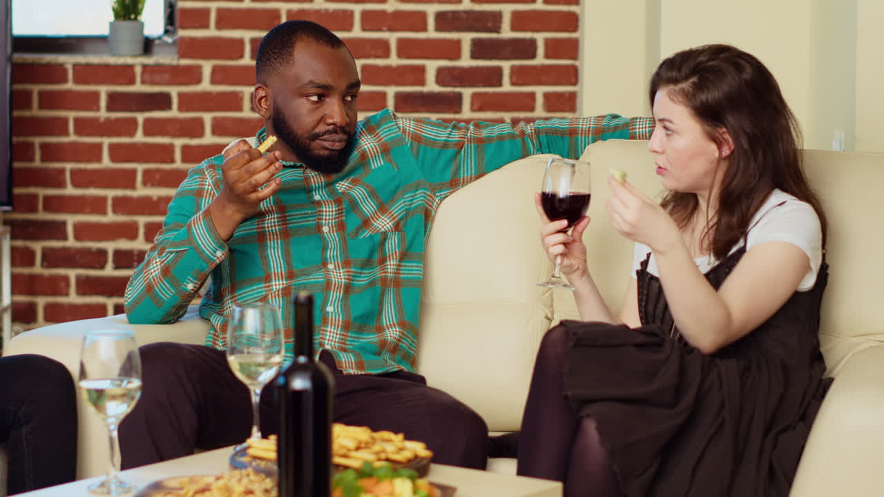 Man flirting with woman on couch at apartment party, enjoying conversation