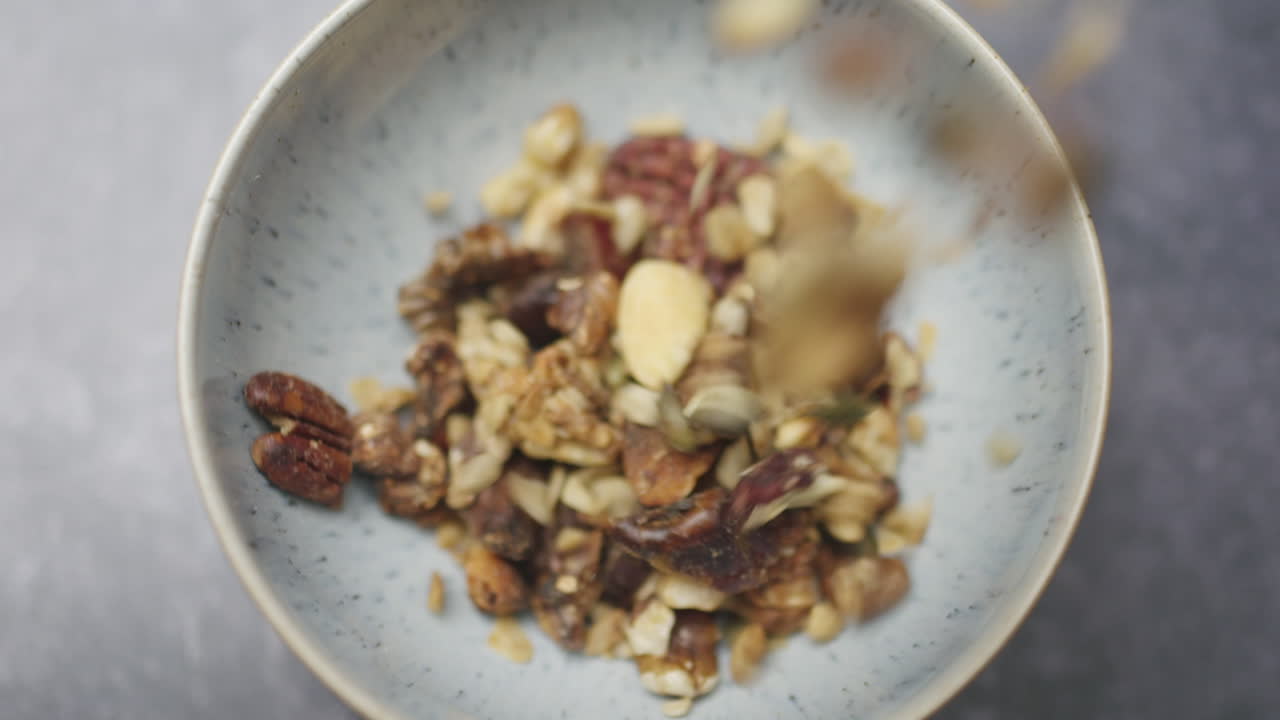 Granola Biologica Salutare, Primo Piano di Marco, Granola Salutare Vegetariana Vegana, Frutta Secca Cruda, Granola che Cade in una Ciotola al Rallentatore