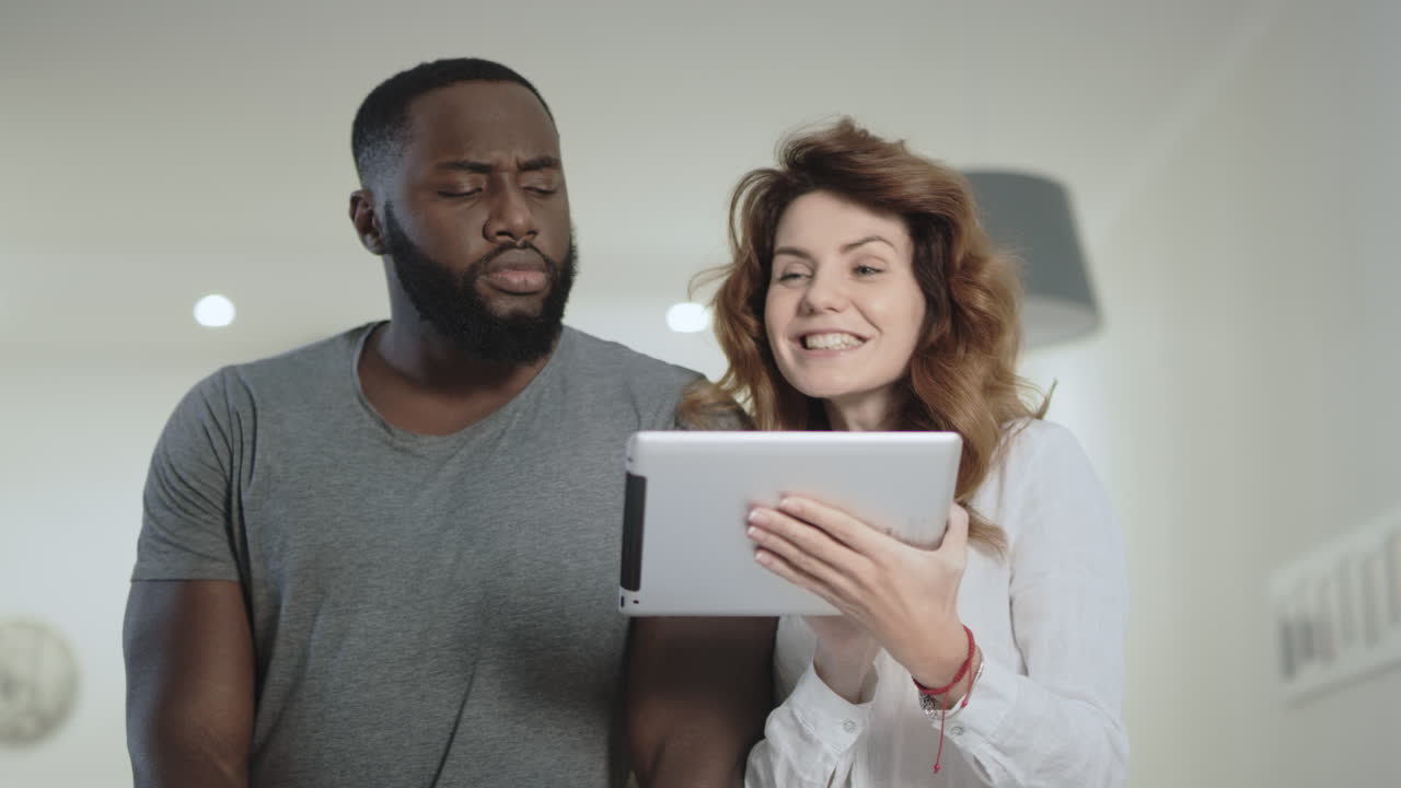 una joven pareja de pie en la sala de estar con la tableta juntos.