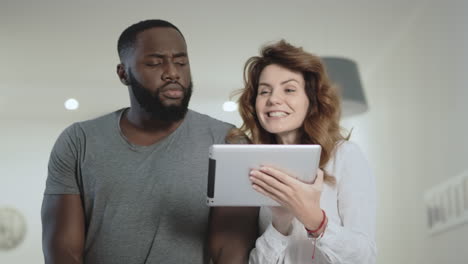 Young-couple-standing-at-living-room-with-tablet-together.