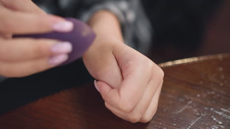 close-up partial view of lady tapping liquid foundation from hand using beauty sponge, smooth blending technique creates flawless, natural finish, emphasizing careful makeup application