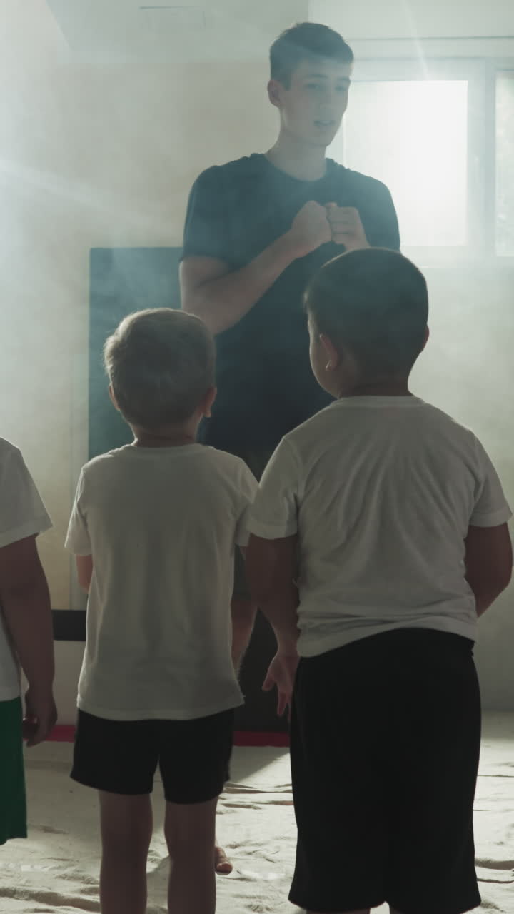 체육관에 있는 아이들에게 권투 자세를 보여주는 트레이너. 관심 있는 어린 학생들은 스모키 클럽에서 운동하기 전에 센세이의 지시를 듣는다.