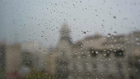 Imágenes-En-Cámara-Lenta-De-Gotas-De-Lluvia-Vistas-A-Través-De-Una-Ventana-Durante-Fuertes-Lluvias,-Con-Un-Paisaje-Urbano-De-Fondo