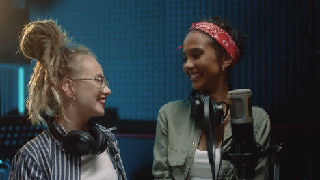 portrait shot of the young cheerful pretty girls, singer of the duo, laughing, looking at each other and then to the camera in the sound studio during recording