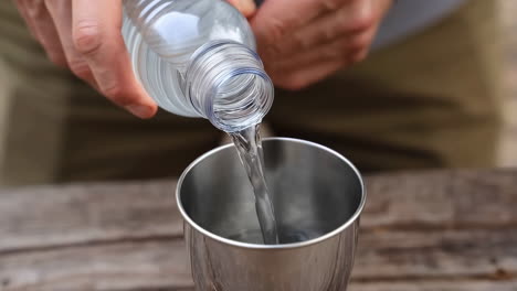 person pouring water from a plastic bottle into a metal cup