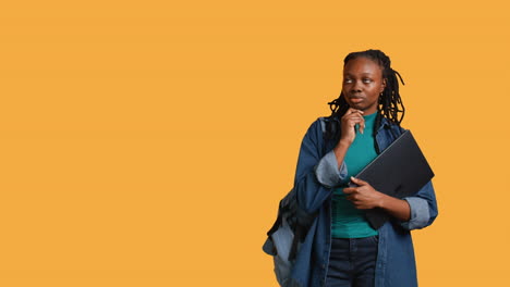 pensive woman carrying laptop, doing thinking gesture, studio background