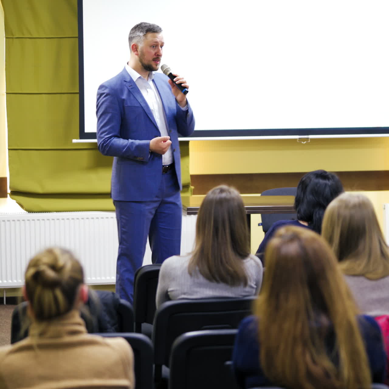 Successful speaker at business forum. Businessman in elegant blue suit is having a talk on podium at business conference. Audience listen to a manager in conference hall.