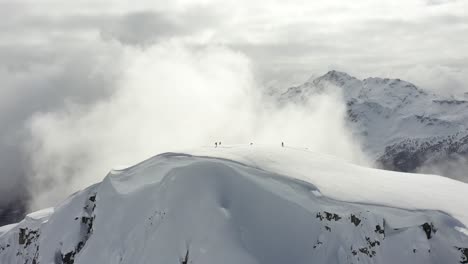 very cinematic shot of backcountry skiers on the top of a snowy mountain in british columbia