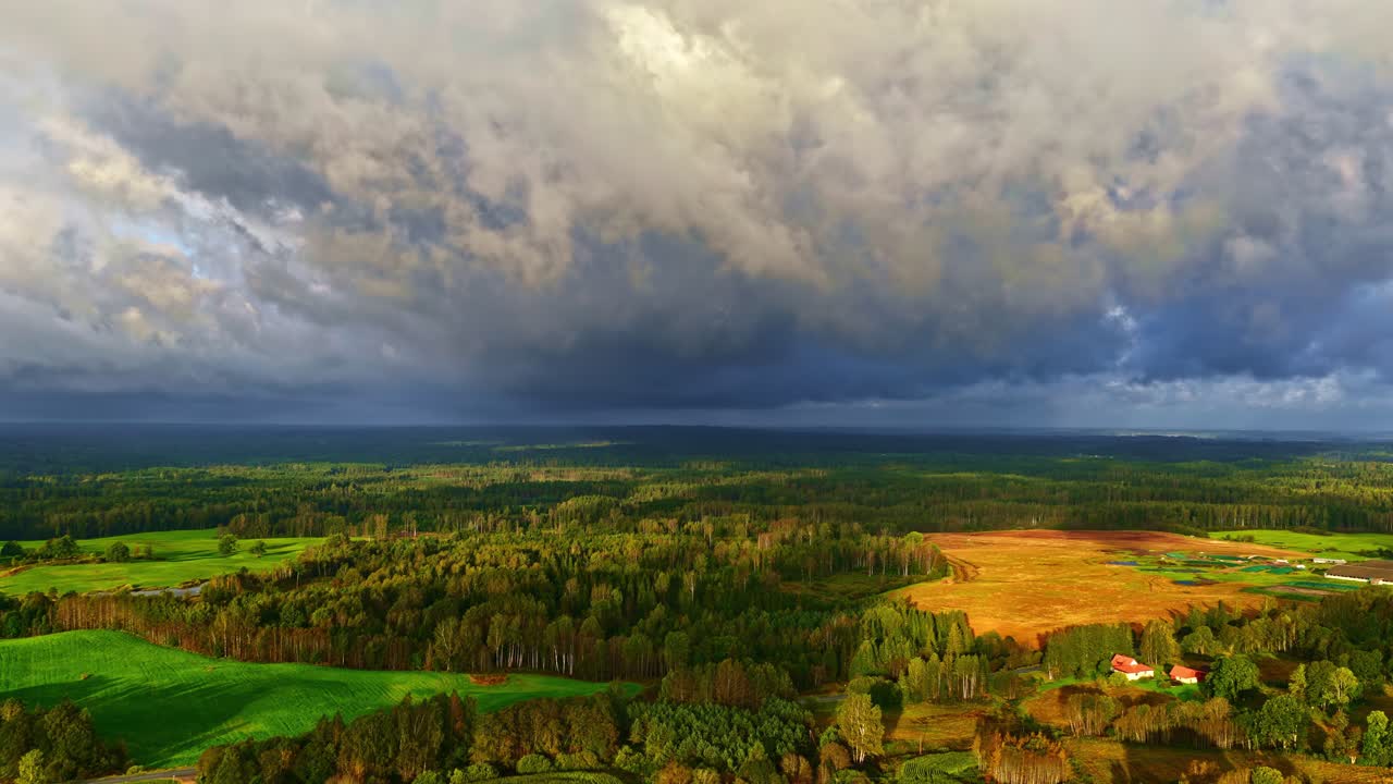 Aerial view of open fields and forest with dramatic storm clouds drifting across the sky