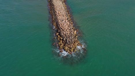 Rocky-breakwater-in-turquoise-waters-near-sitges,-spain,-aerial-view