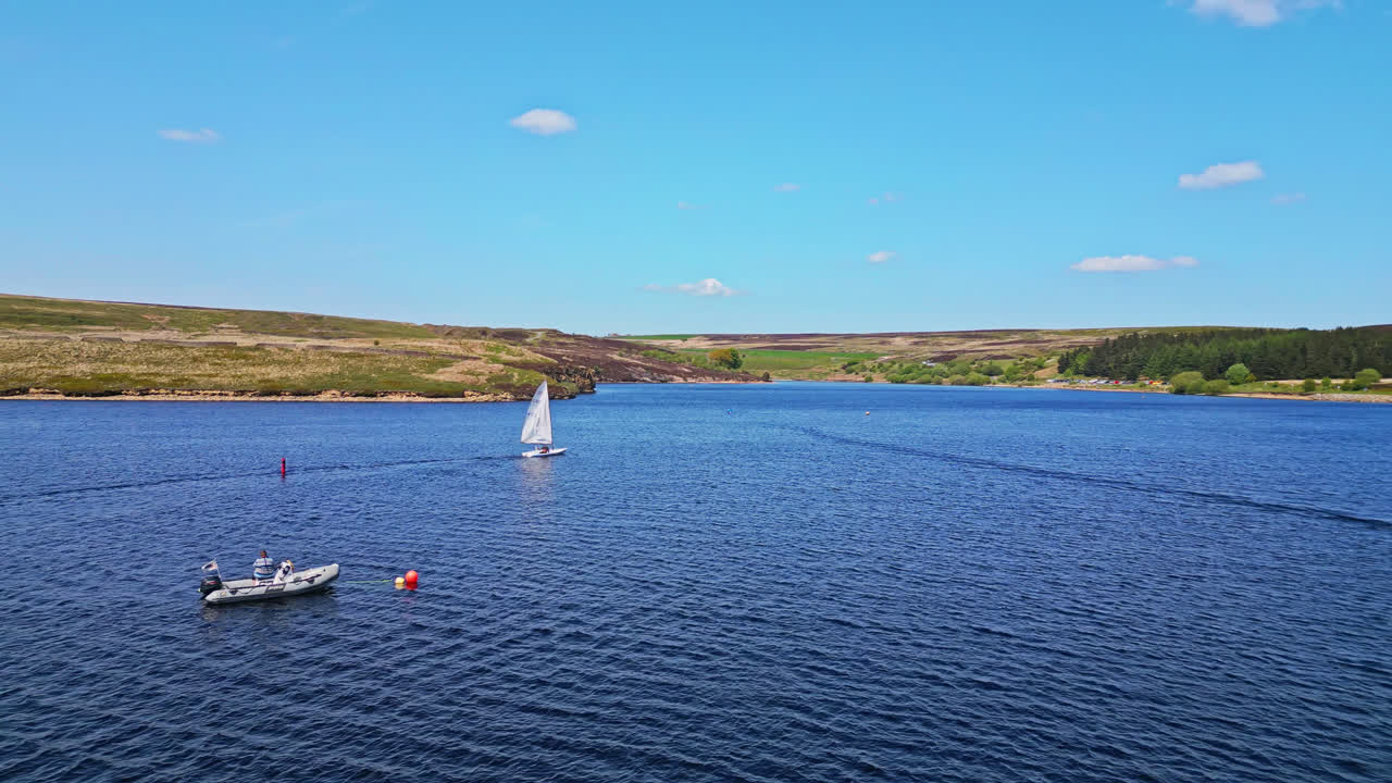el embalse de winscar en yorkshire sirve de telón de fondo para un evento deportivo de fin de semana, donde los entusiastas de la vela se entregan a una emocionante carrera de barcos con sus pequeños barcos de un solo hombre