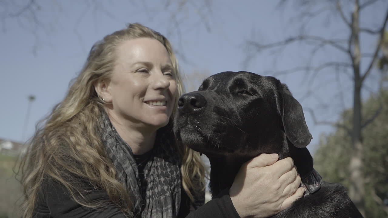 Smiling Woman pets her black labrador dog at the park (Cinematic)