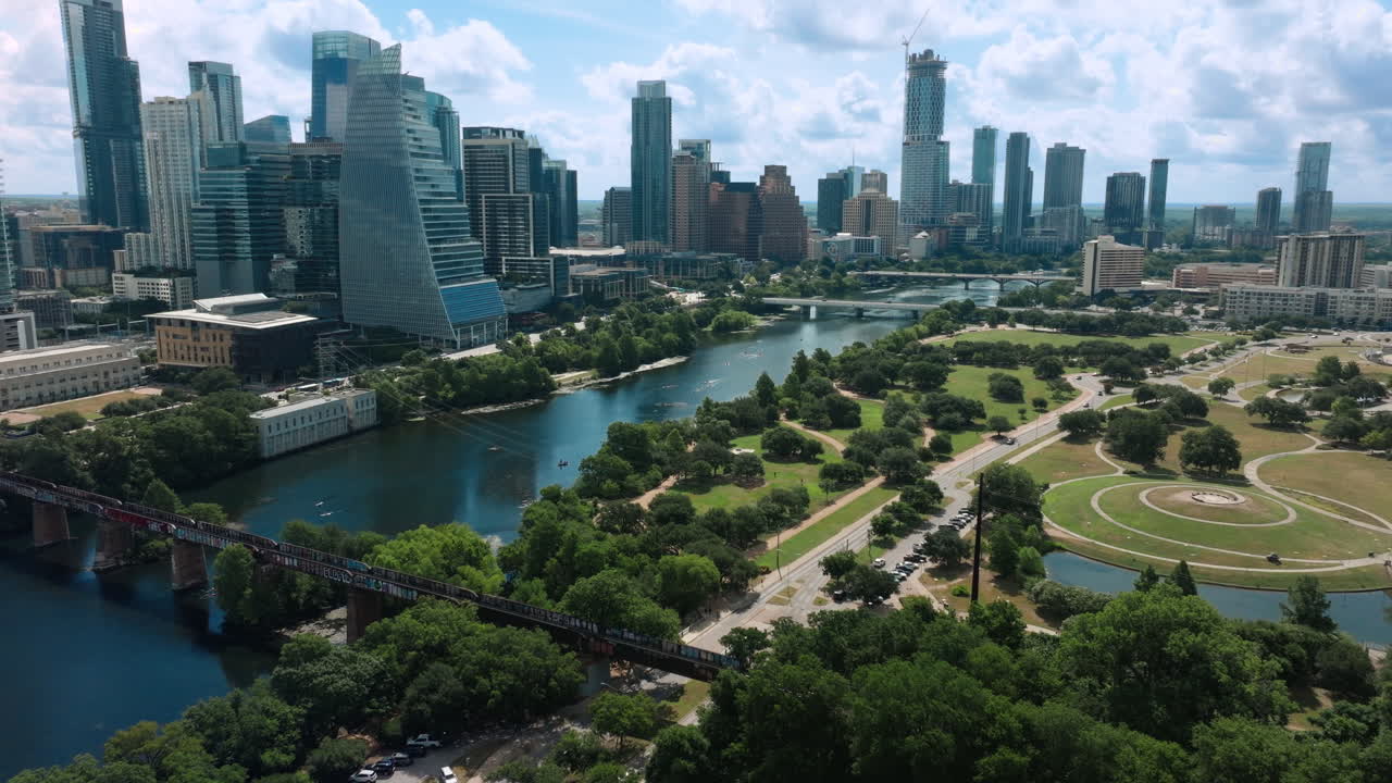 Daytime drone shot captures Auditorium Shores, Lady Bird Lake, and the full Austin skyline on a beautiful blue-sky day. Clear air, bright light, and vibrant colors of scenic city view