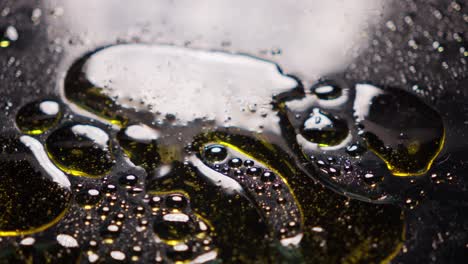 Golden-oil-drips-into-black-liquid-forming-bubbles-in-an-abstract-close-up-shot