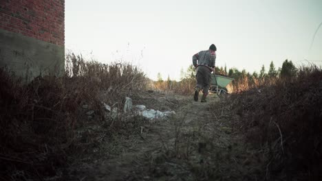 un hombre utilizando una carretilla para transportar tierra, con un perro en el fondo - toma estática