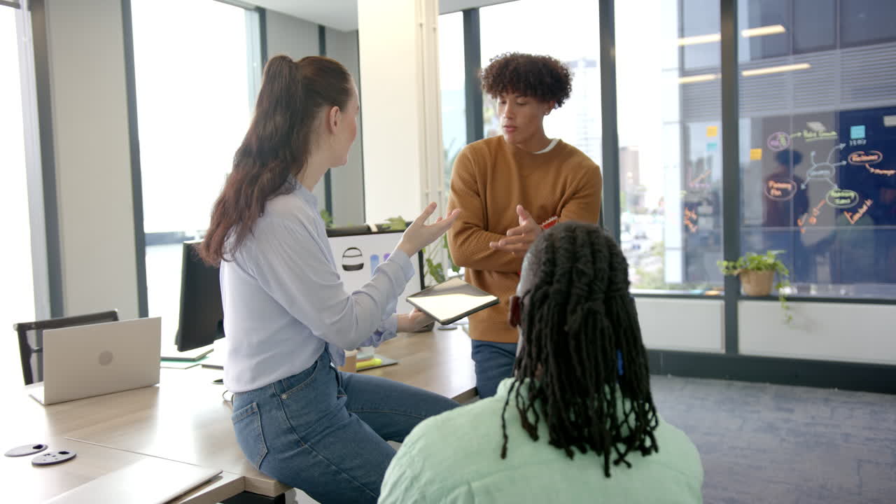 Collaborating with tablet and laptop, diverse colleagues discussing work in modern office
