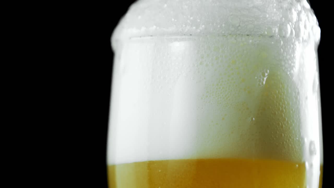 Birra versata in un bicchiere su sfondo nero 4k