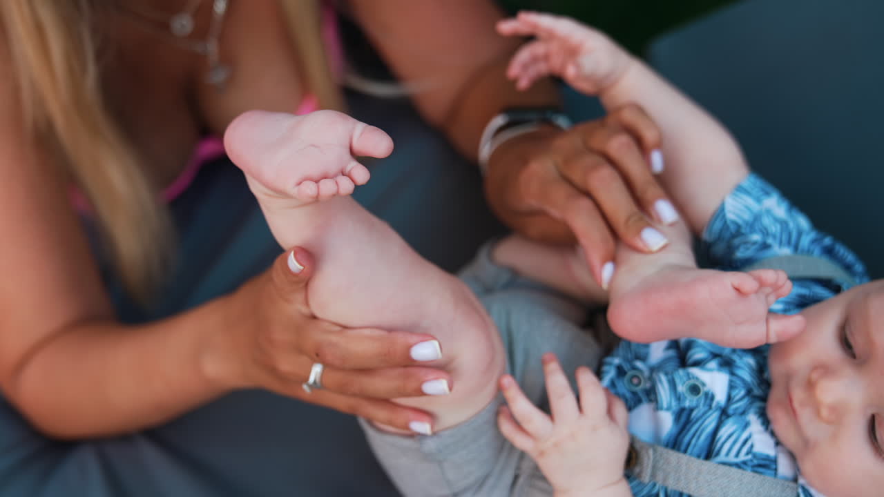 Unrecognized woman with her baby boy. Mother is playing with her cute infant wearing shirt and shorts.