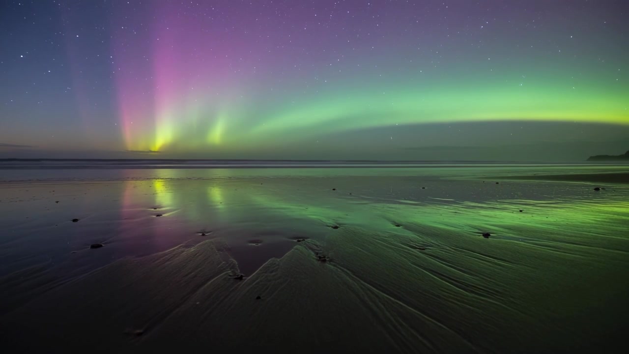 Merekam busur aurora yang bergeser di atas pantai pada malam hari, menampilkan tirai magenta dan variasi lambat.