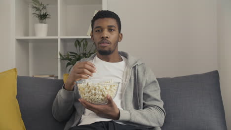 young man watching attentively a movie and eating popcorn 1