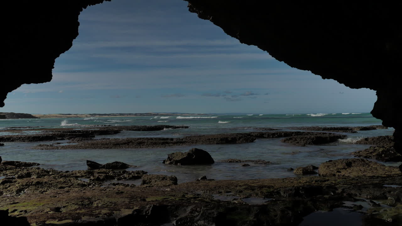 tiro inclinado desde la cueva, que revela la costa y las olas, con un niño caminando por el marco
