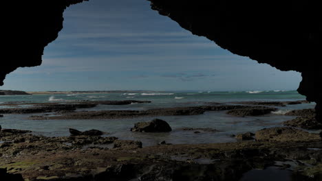 tilt-up shot from cave, revealing coastline and waves, with child walking across frame