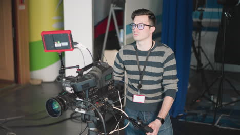 camera operator focused while adjusting camera with monitor on set. filming equipment setup in tv studio environment with cables and professional gear