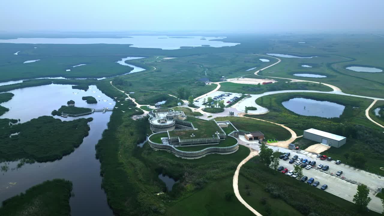 Hazy, humid aerial orbits descends as birds pass over wetlands modern environmental building