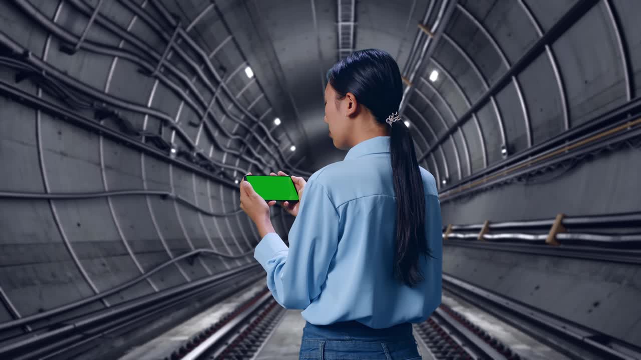Back View Of Asian Female In Underground Subway Tunnel, Checking On Smartphone With Green Screen And Look At The Subway Tunnel