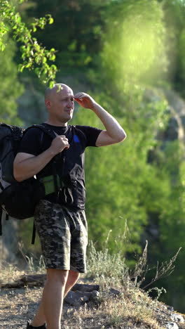 hiker male looks at the beautiful landscape on the natural green background. a tourist man with a rucksack standing on the hill and admires the nature in a sunny day vertical video