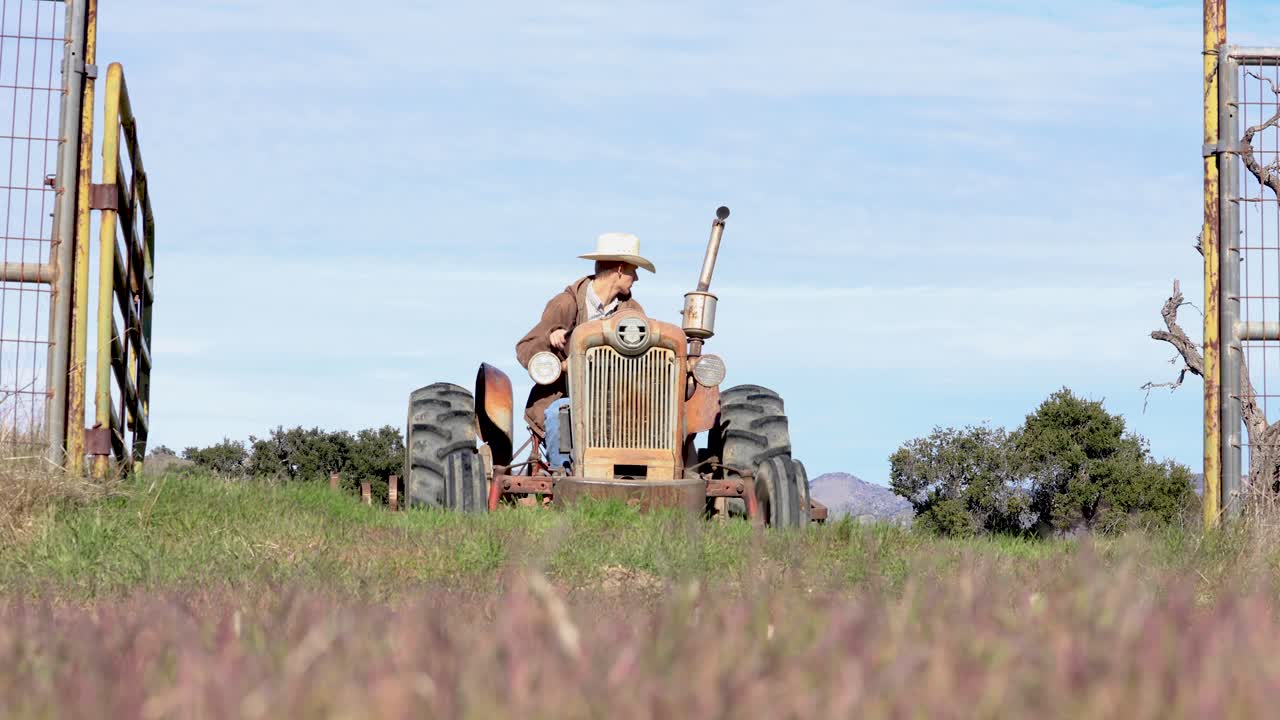 Rancher Towing Harrow Through Fence on Farming Field